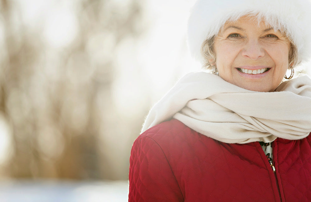 Femme mature en plein hiver qui sourit et est en pleine santé car elle booste son immunité et renforce son système immunitaire