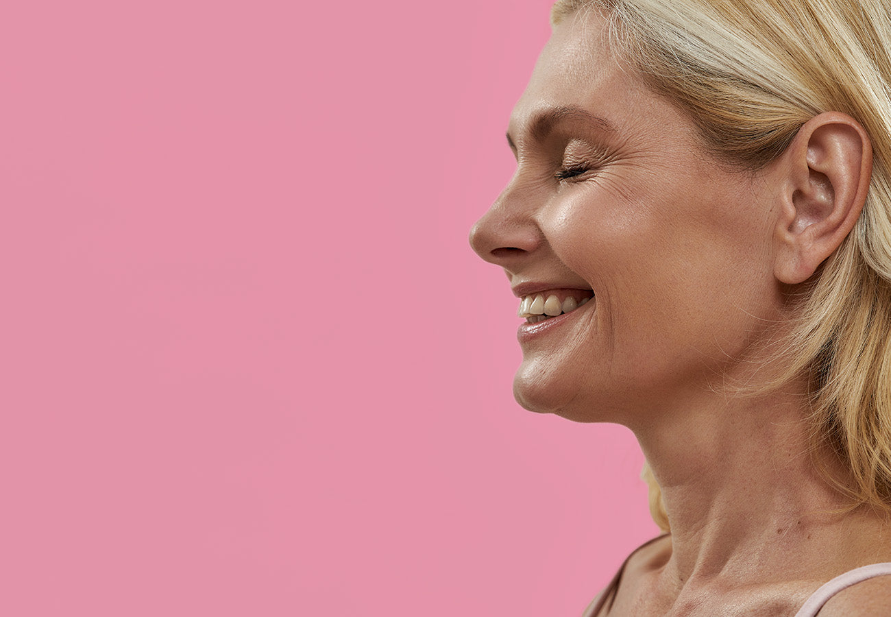 Jolie femme souriante et épanouie sur fond rose, illustrant les bienfaits du Booster Ventre Léger des Boosters Naturels pour améliorer le confort digestif et favoriser un bien-être naturel