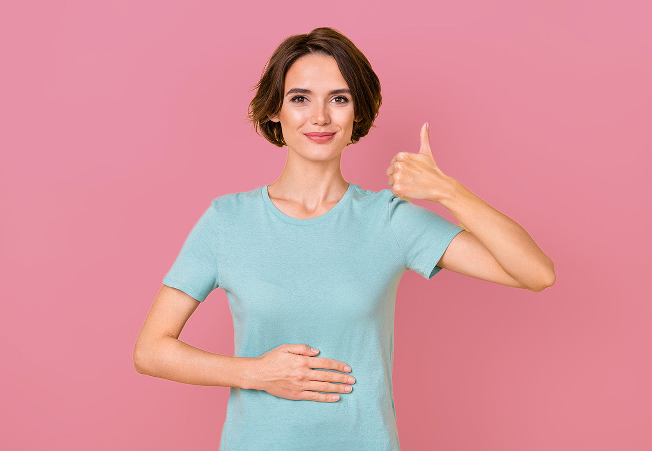 Femme souriante touchant son ventre et montrant un pouce en l'air, illustrant le bien-être digestif apporté par le Booster Ventre Léger des Boosters Naturels, complément naturel pour améliorer la digestion et réduire les ballonnements